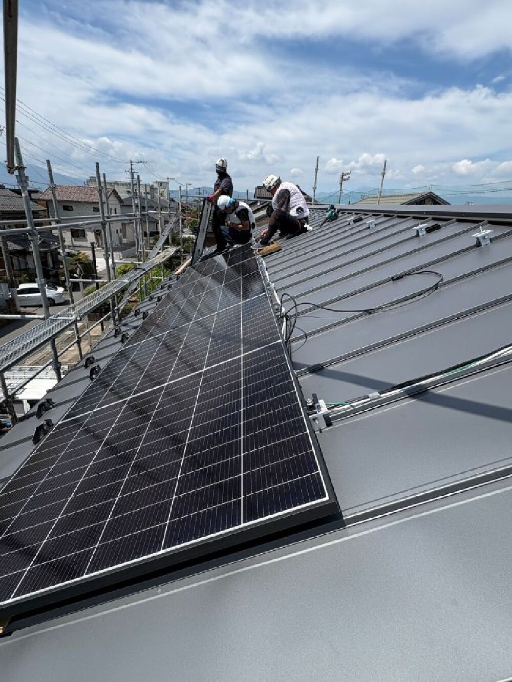 大垣市I様邸の金属屋根に、専用の取り付け金具を使用して太陽光発電パネルを設置している工事中の様子