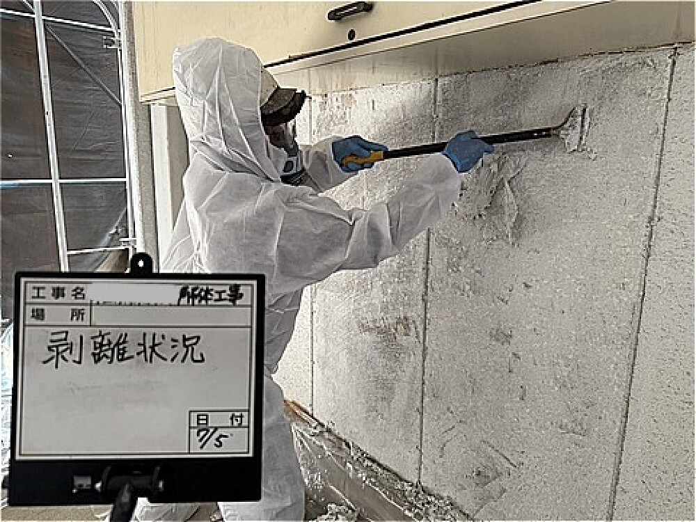 防護対策を行いながら手作業で仕上げ材を除去する解体工事の様子